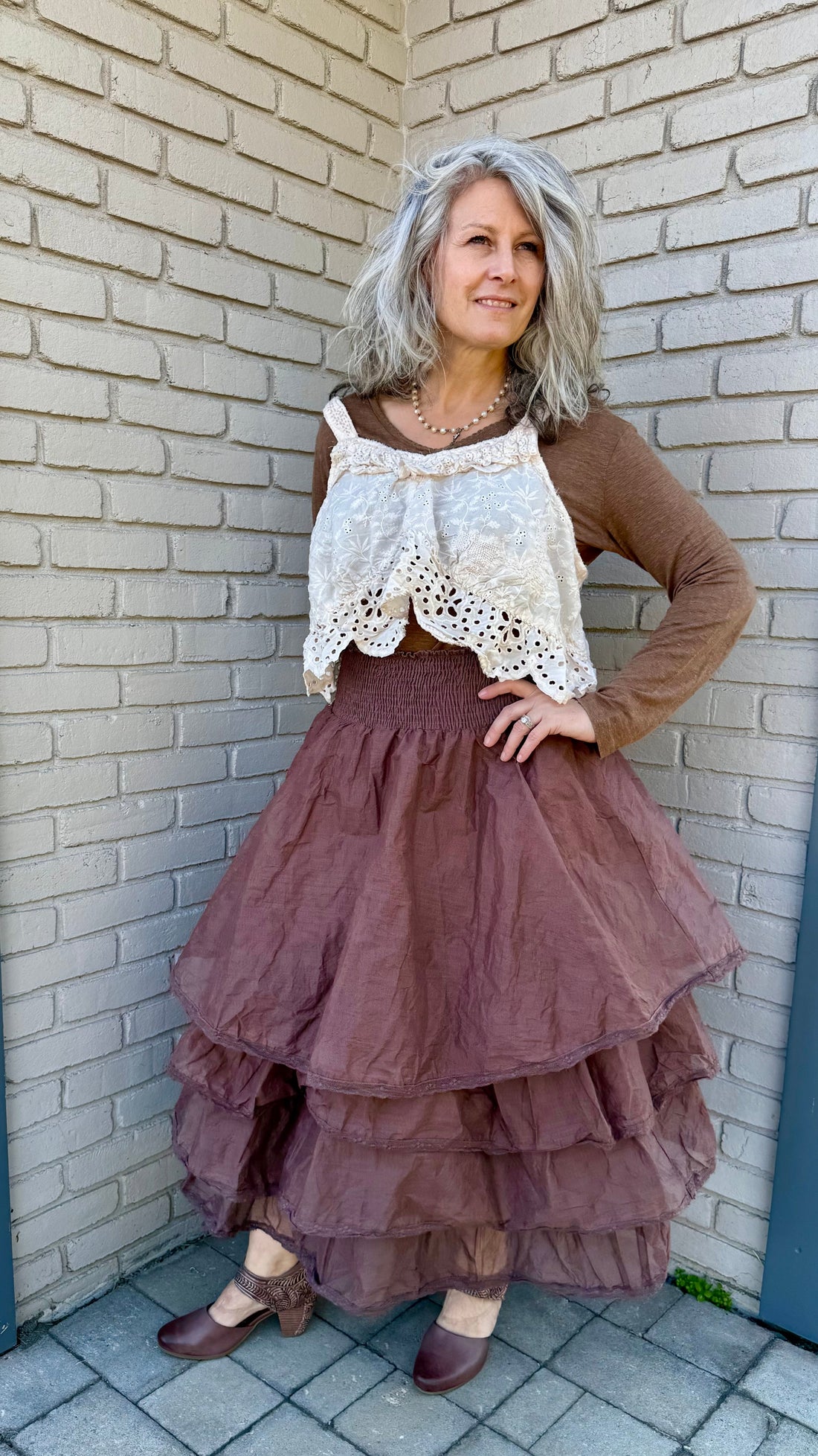 Woman in a layered dress standing against a brick wall