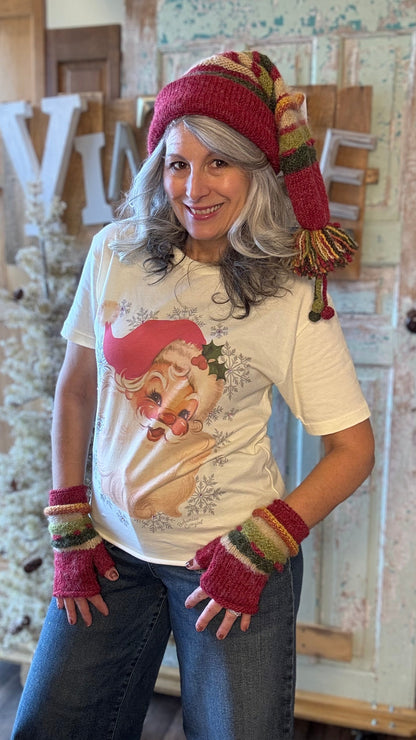 Person wearing a festive outfit with a Santa Claus shirt, hat, and gloves in a home setting.