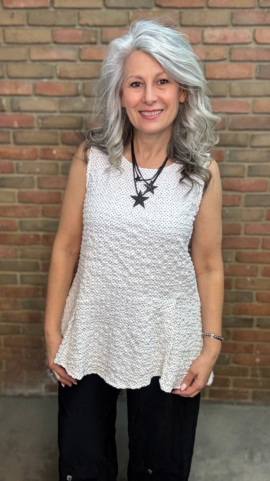 Woman wearing Lyndon Tank - Polka Dot and black pants against a brick wall.