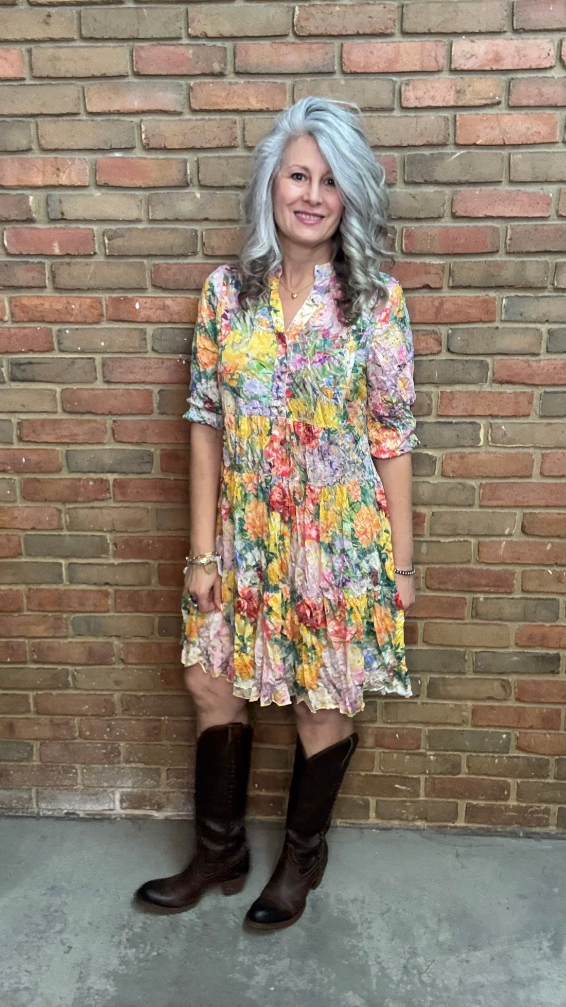 Woman in Garden Floral Print Tiered Dress and brown boots standing against a brick wall.