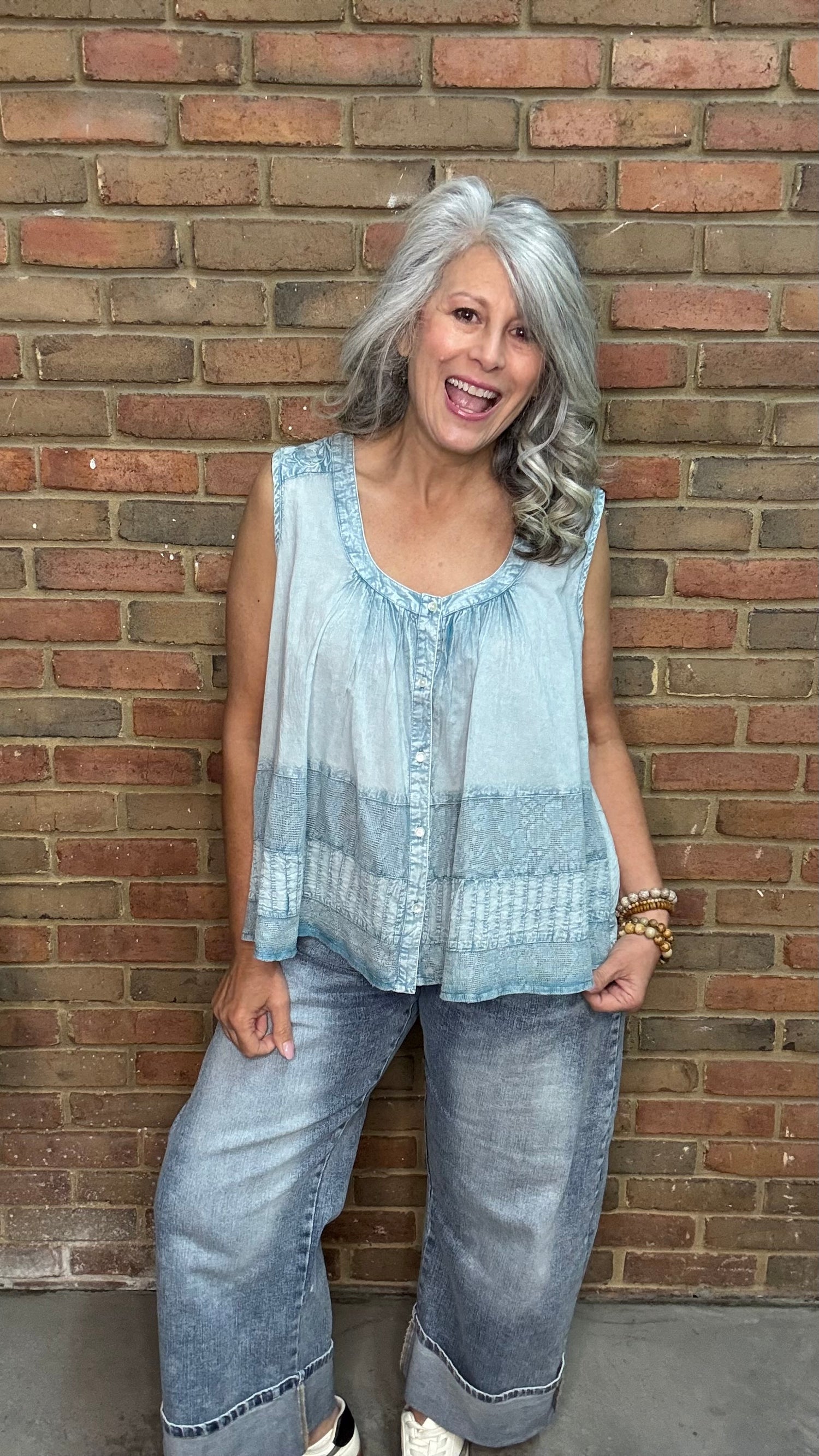 Woman wearing the Denim Blue Crochet Contrast Tank Top, a light blue sleeveless top and jeans standing against a brick wall.