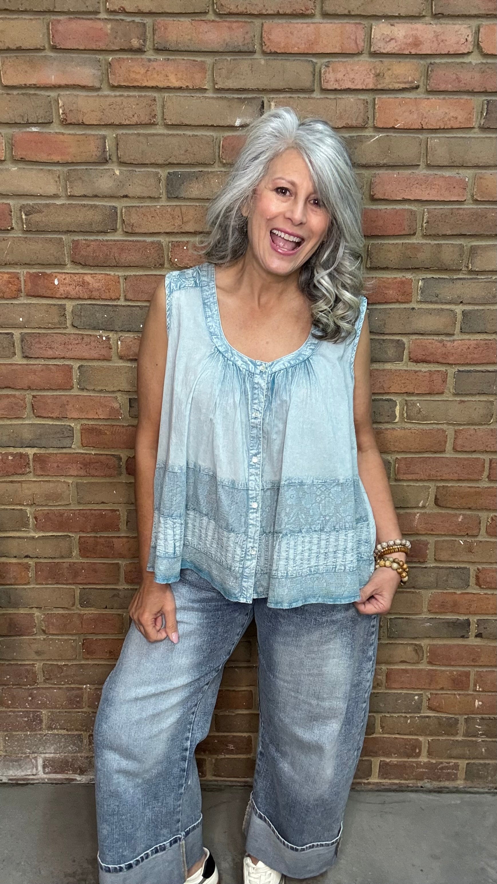 Woman wearing the Denim Blue Crochet Contrast Tank Top, a light blue sleeveless top and jeans standing against a brick wall.