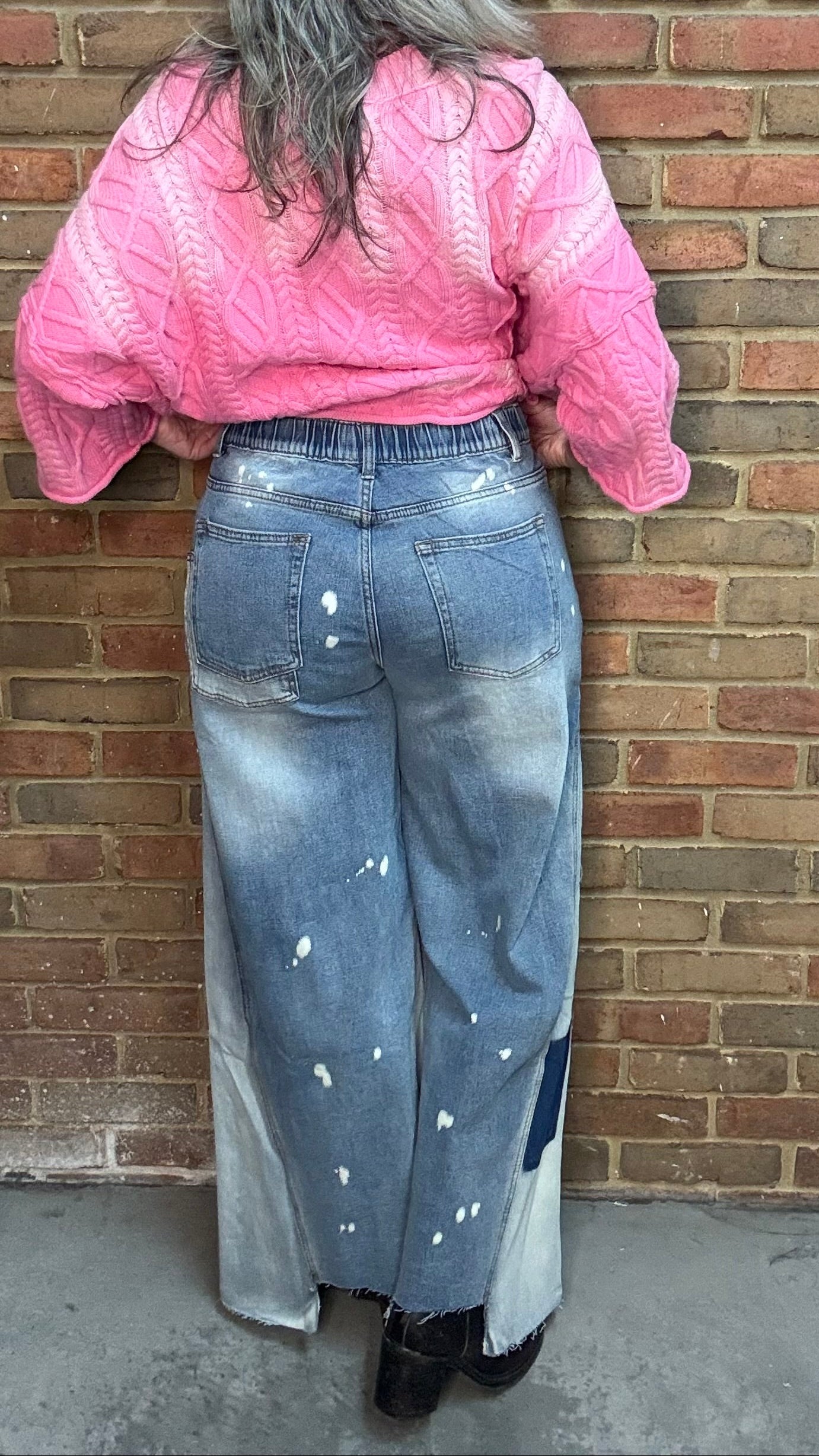 Woman wearing Bleached Wide Leg Jeans and Dusty Pink Ombre Sweater standing against a brick wall.