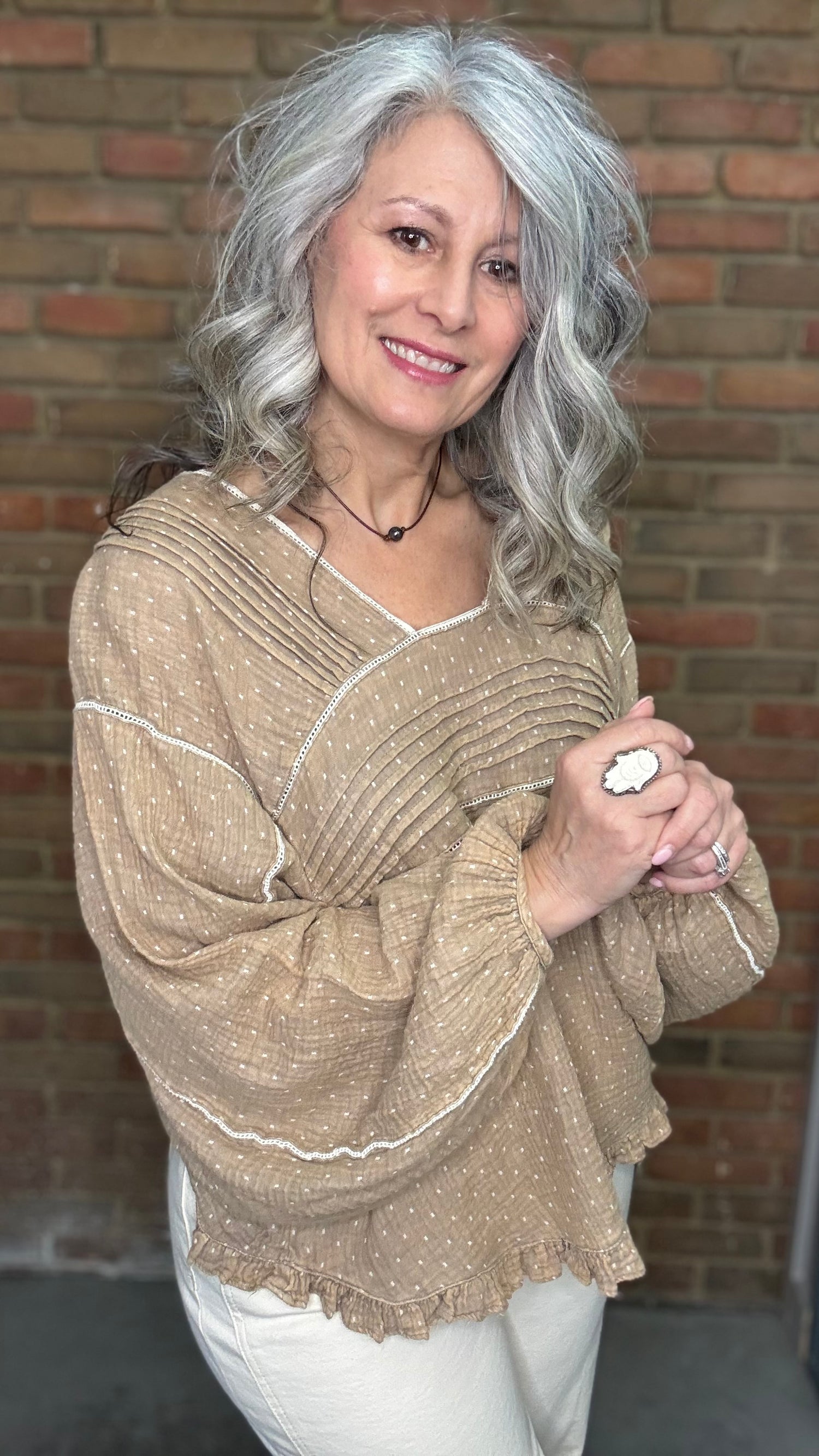Woman wearing Mocha and Ivory Print Long Sleeve Top and blue jeans standing against a brick wall.