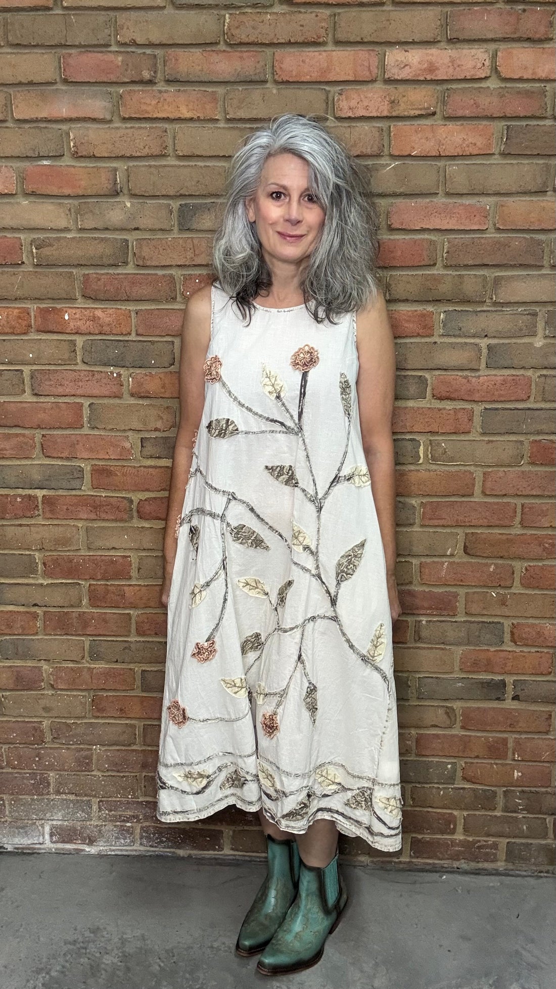 Woman in a white floral dress standing against a brick wall.
