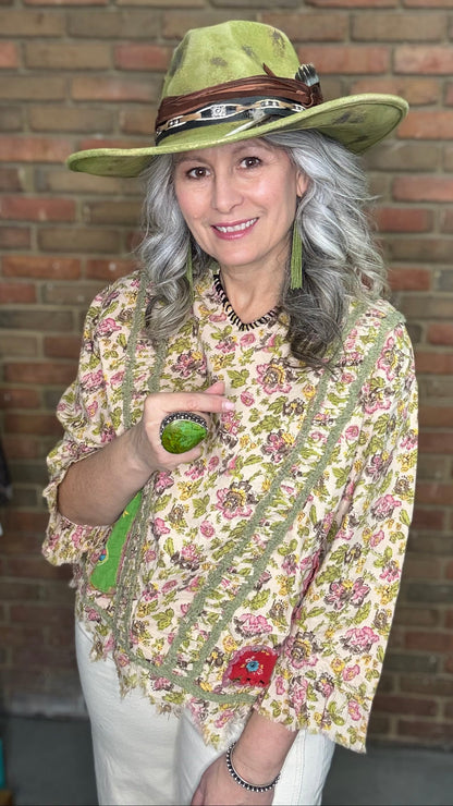 Woman wearing Desert Winds Top and wide-brimmed hat against a brick wall.