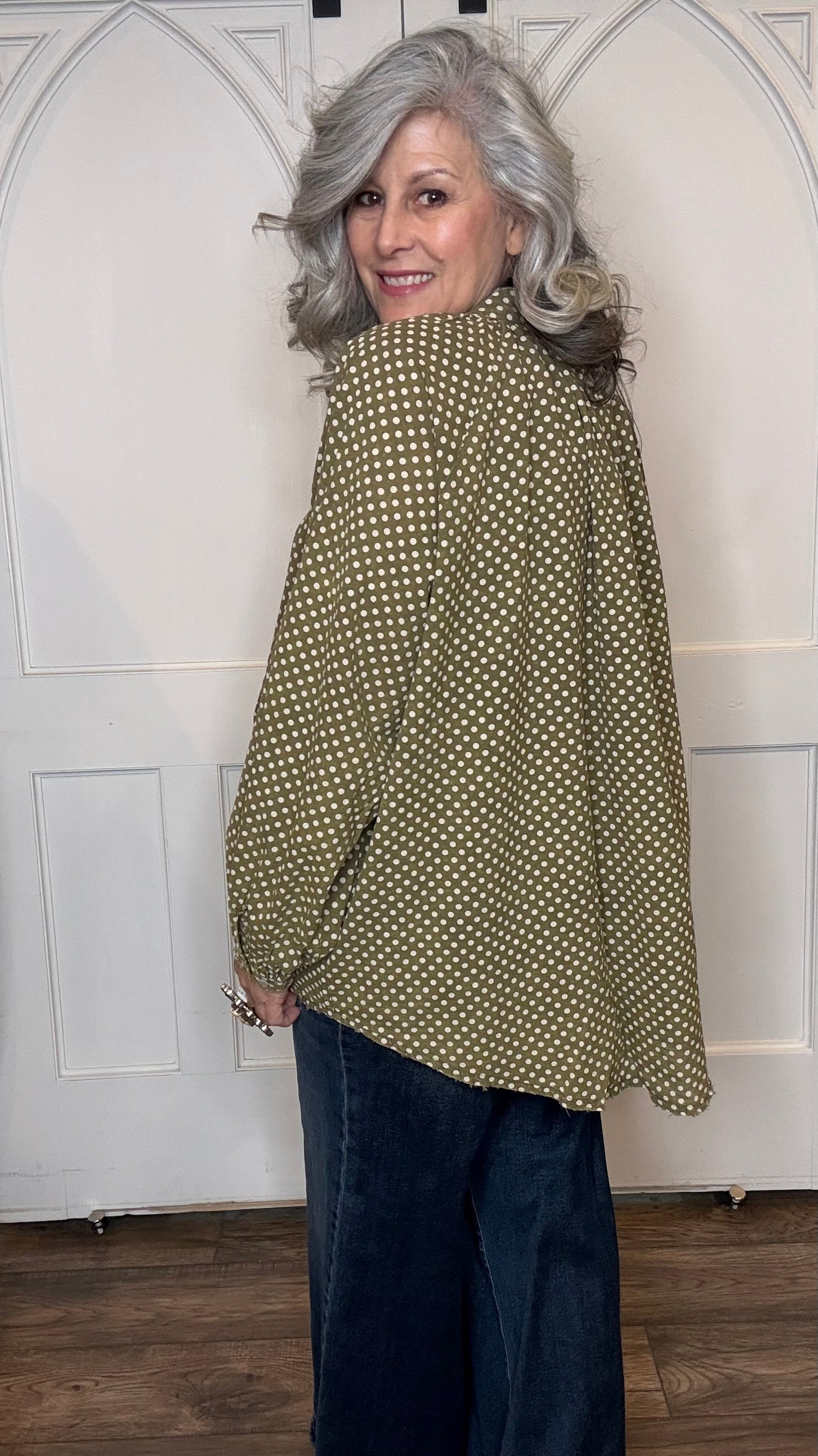 Woman wearing the Sweet Nothings Top-Olive Dot and Judy Blue Palazzo jeans standing against a white paneled wall.
