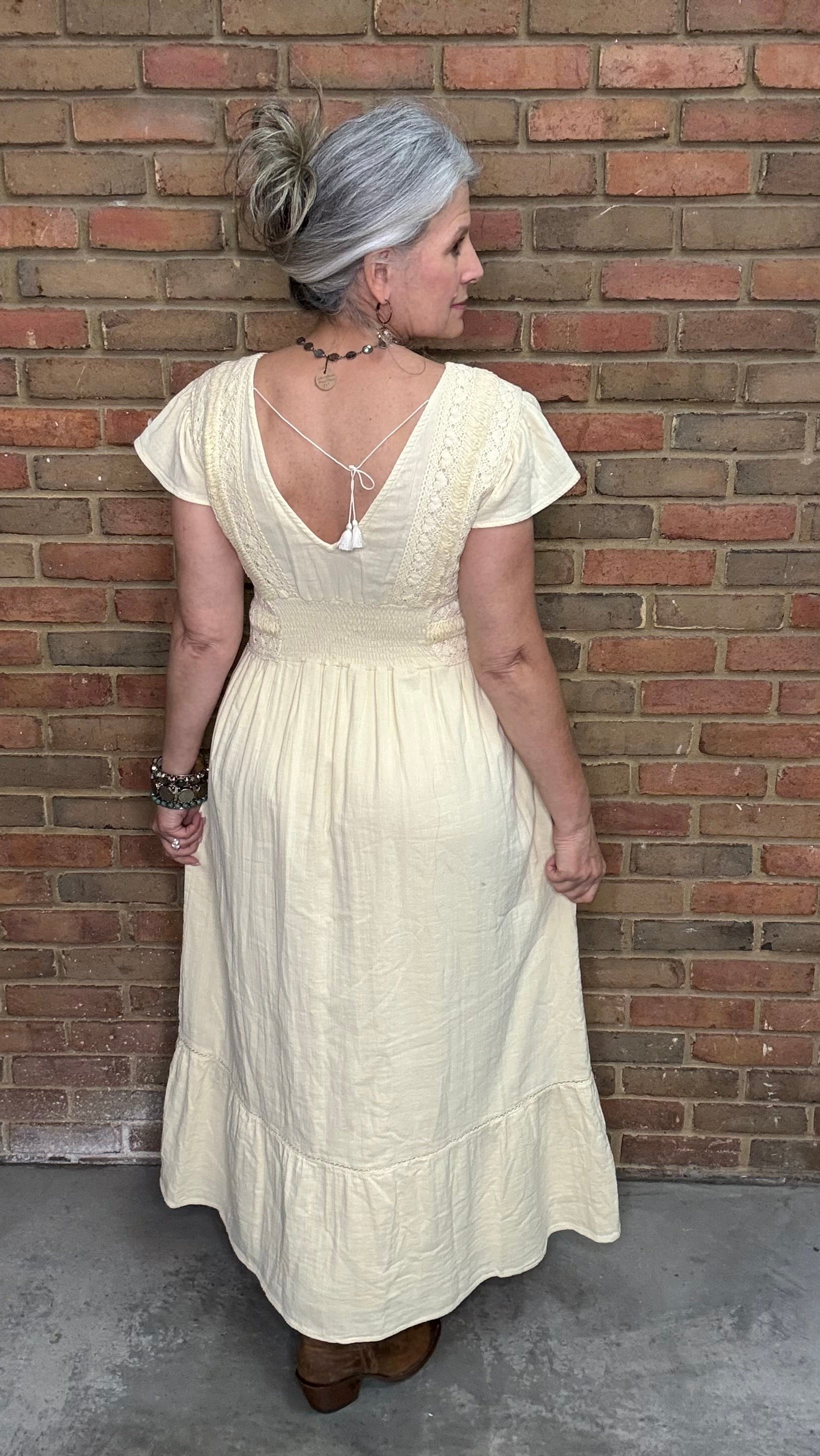 Woman in the Vina Cotton Lace Dress in Ivory standing against a brick wall