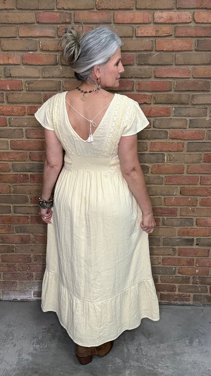 Woman in the Vina Cotton Lace Dress in Ivory standing against a brick wall