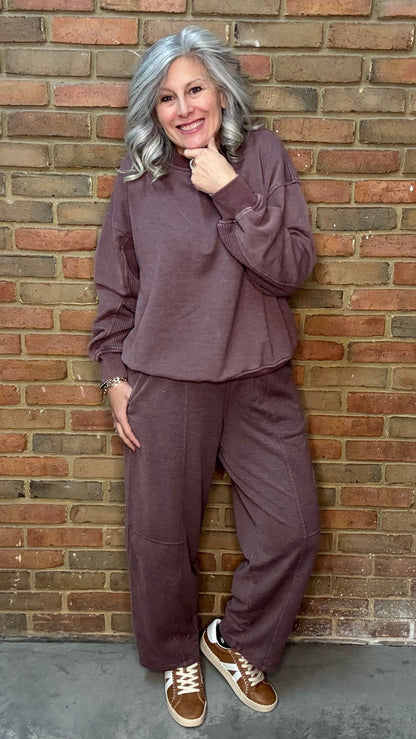 Person wearing a brown outfit leaning against a brick wall