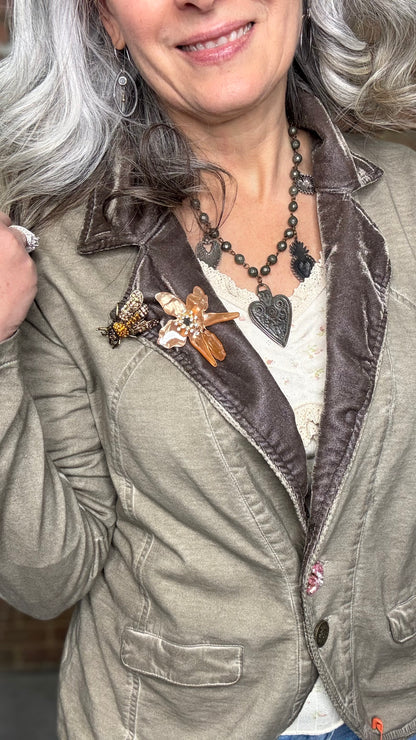 Woman wearing the Colonel Jacket in Taupe with a Sacred Heart Charm Necklace standing in front of brick wall.