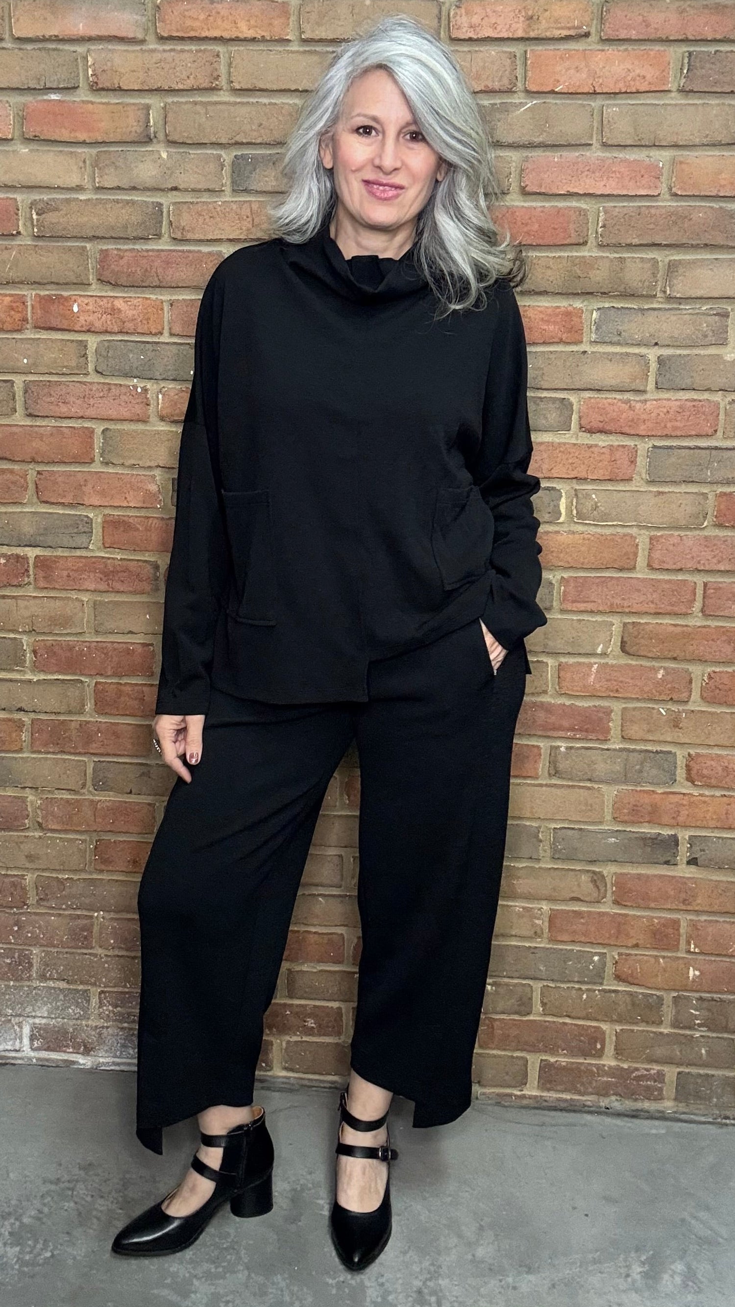 Woman in black outfit standing against a brick wall