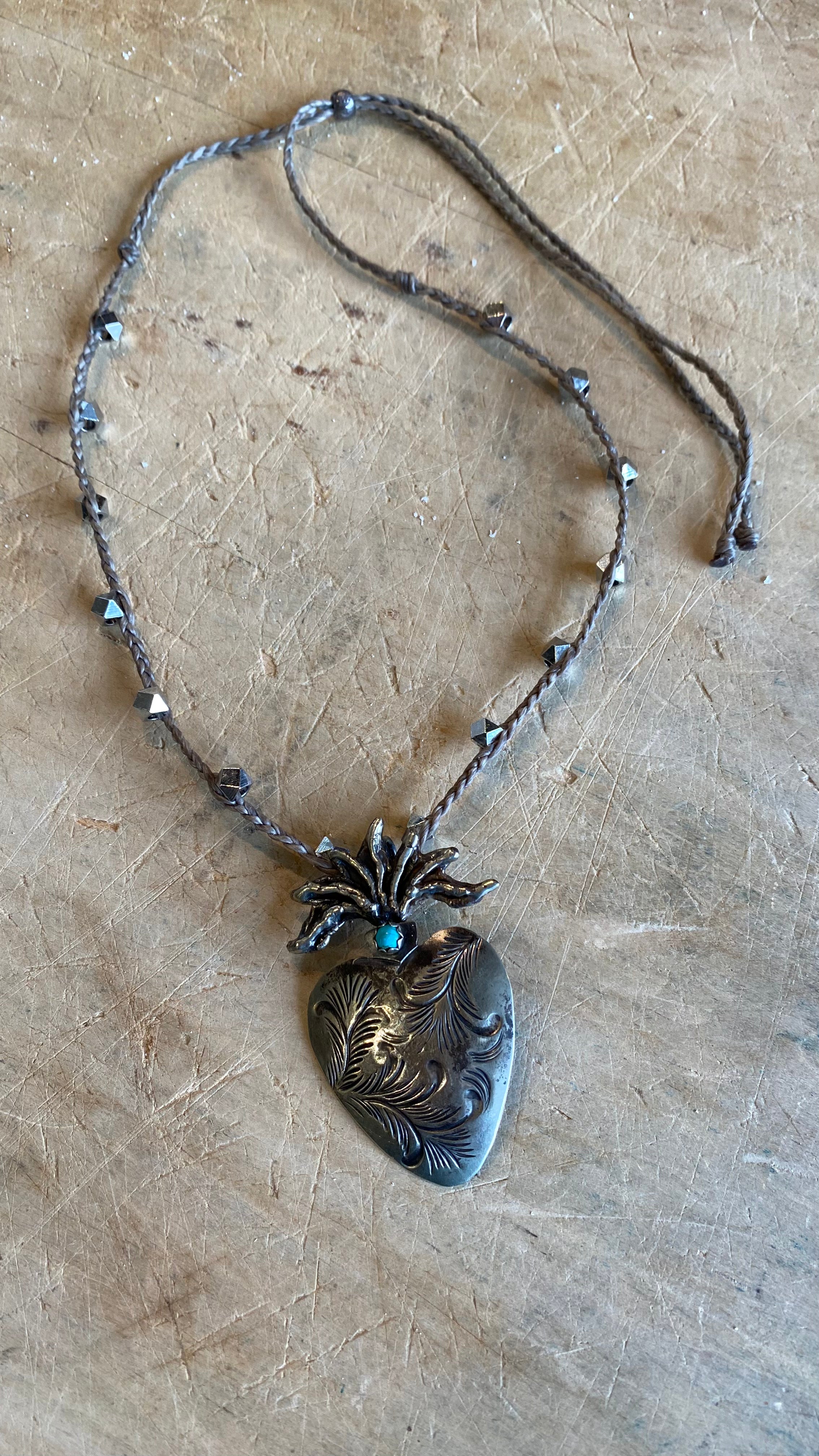 Carved Silver Heart with Turquoise Necklace against a light wooden background