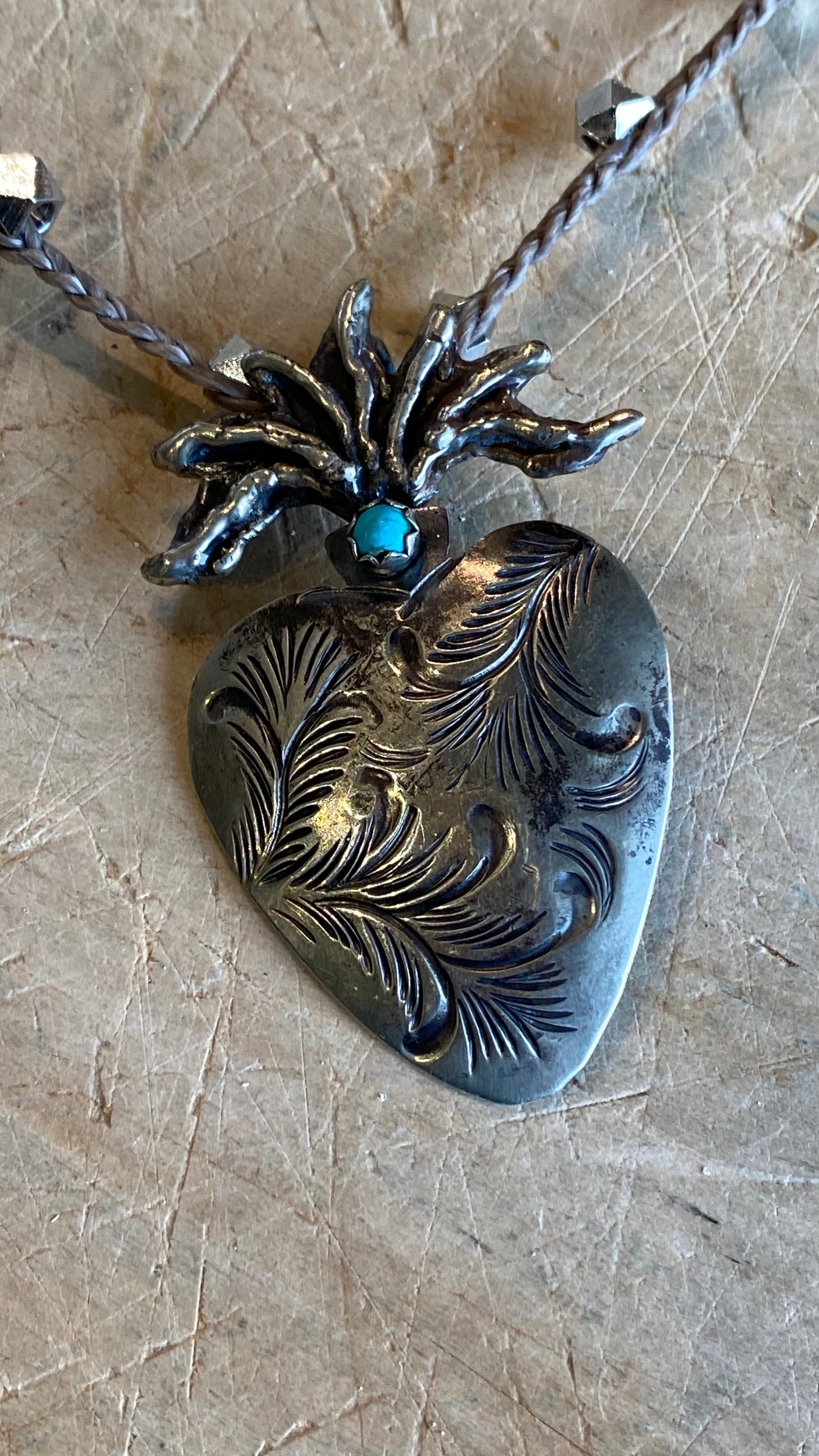 Carved Silver Heart with Turquoise Necklace against a light wooden background