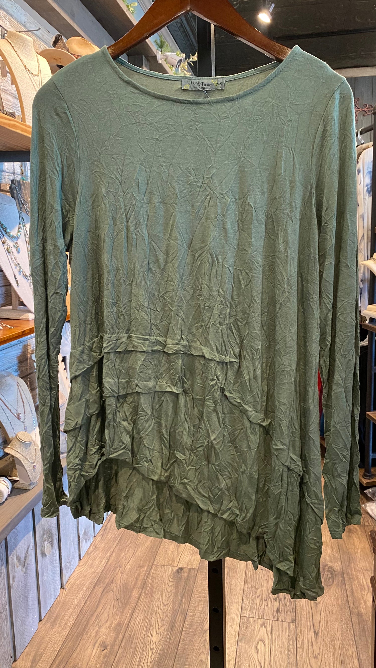Green long-sleeved top with an asymmetrical hemline and round neck displayed on a mannequin.