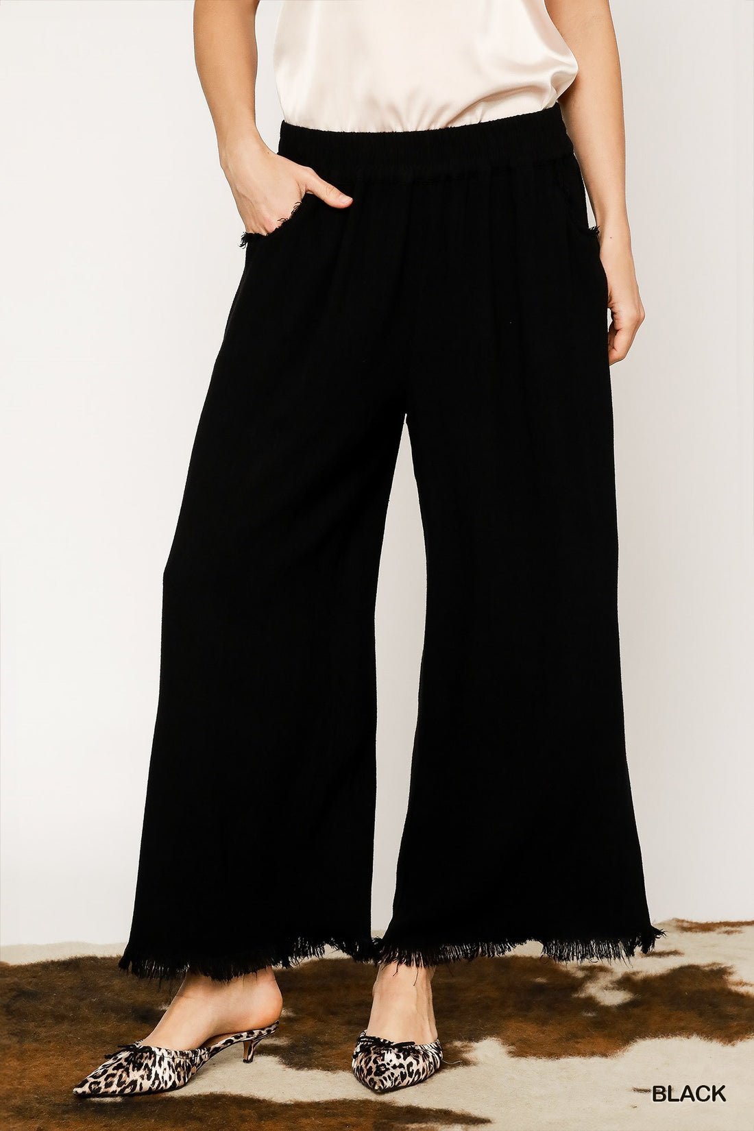 Person wearing black wide-leg pants with a white top and leopard print shoes on a plain background