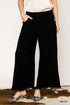 Person wearing black wide-leg pants with a white top and leopard print shoes on a plain background