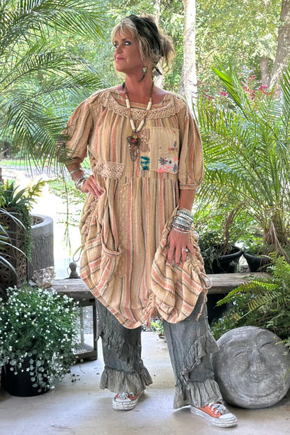 Woman in a flowing dress standing outdoors with greenery in the background