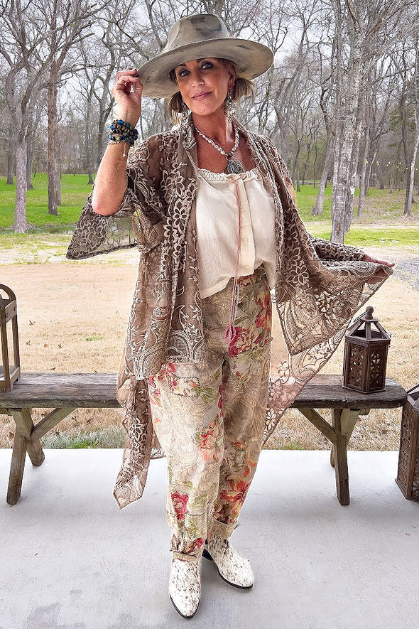 Woman in a stylish outfit with a floral pants, lace jacket, and cowboy boots outdoors.