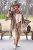 Woman in a stylish outfit with a floral pants, lace jacket, and cowboy boots outdoors.