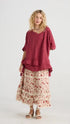 front view of Perdita Cotton Skirt in Dark Rose on a model wearing a long red colored shirt.