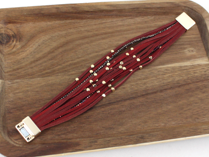 Red beaded bracelet with gold accents on a wooden tray