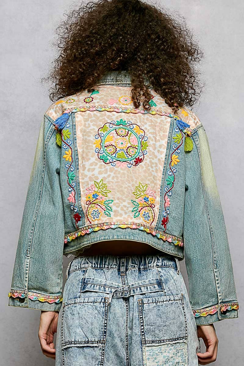 Person wearing a colorful embroidered denim jacket on a gray background