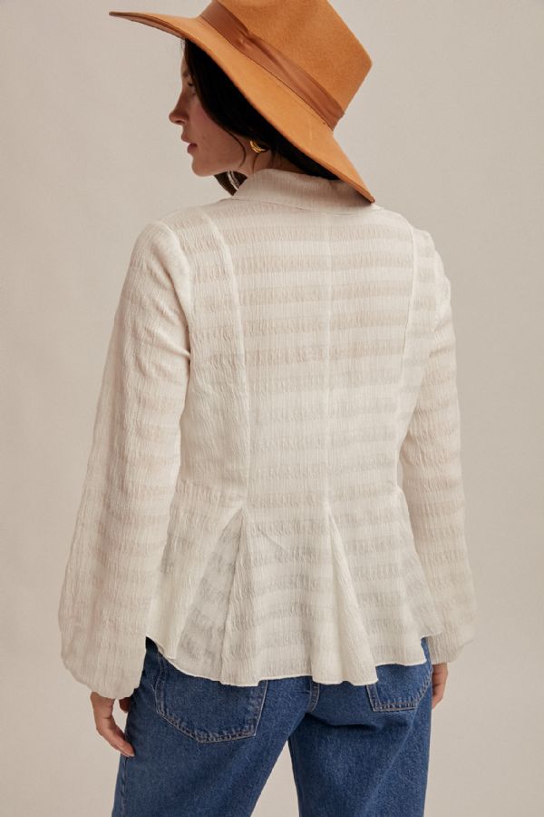 Person wearing a beige textured blouse and brown hat on a plain background