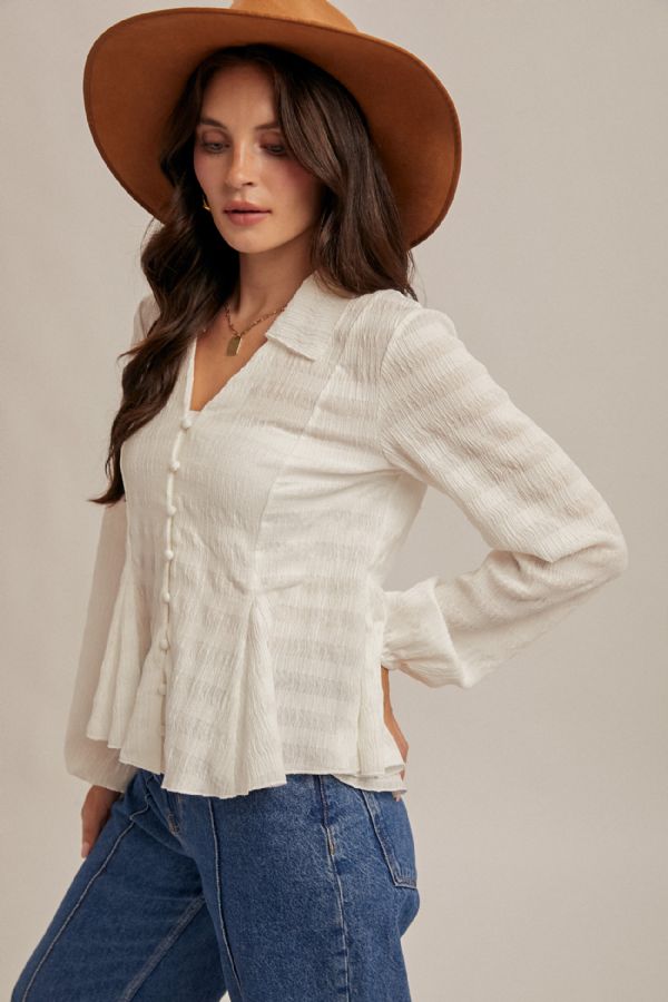 Woman wearing a white blouse, blue jeans, and a brown hat against a plain background