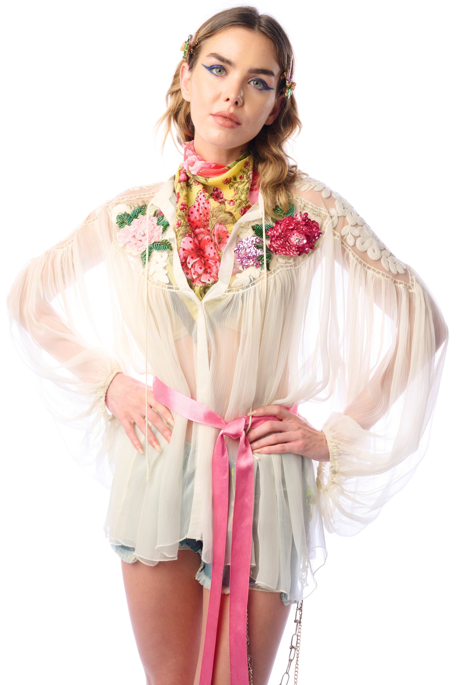 Woman wearing a floral embroidered outfit with a pink belt on a white background